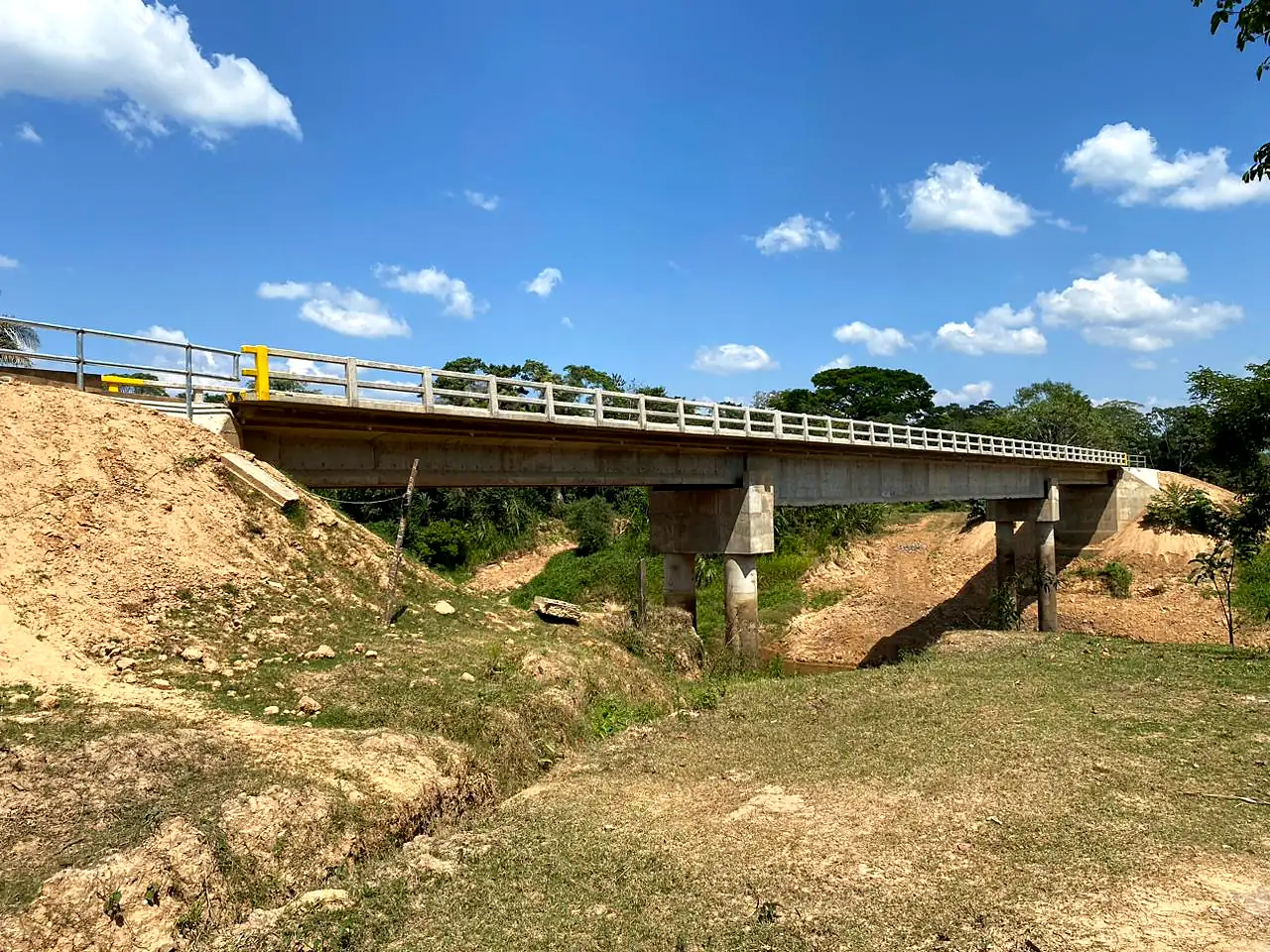 Vista lateral del puente terminado sobre el río Apere, con barandas y defensas amarillas