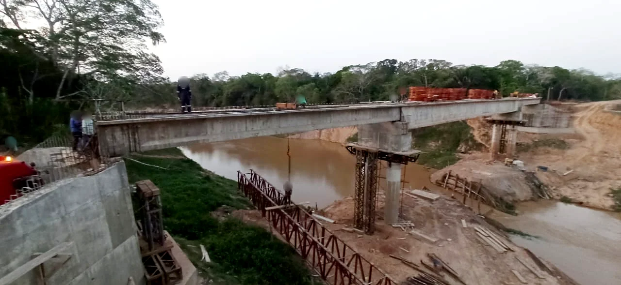 Vigas del tablero sobre el río Apere con la cercha metálica de montaje debajo y personal en el tablero (rostros difuminados)