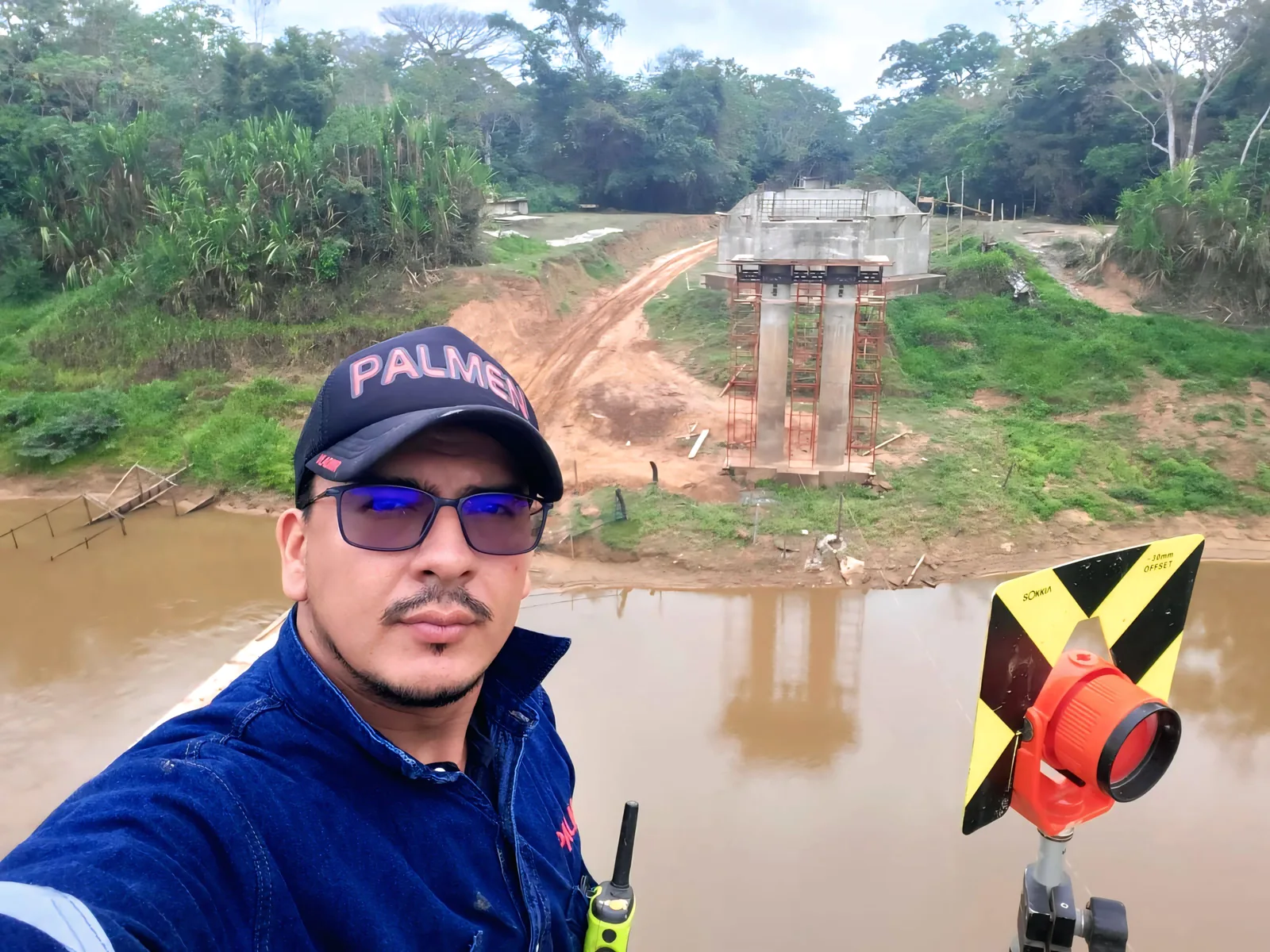 Ing. Vladimir J. Garcia Umaday, fundador de VLAJOGAR, en obra en el puente sobre el río Apere, con una pila al fondo y el prisma topográfico en primer plano