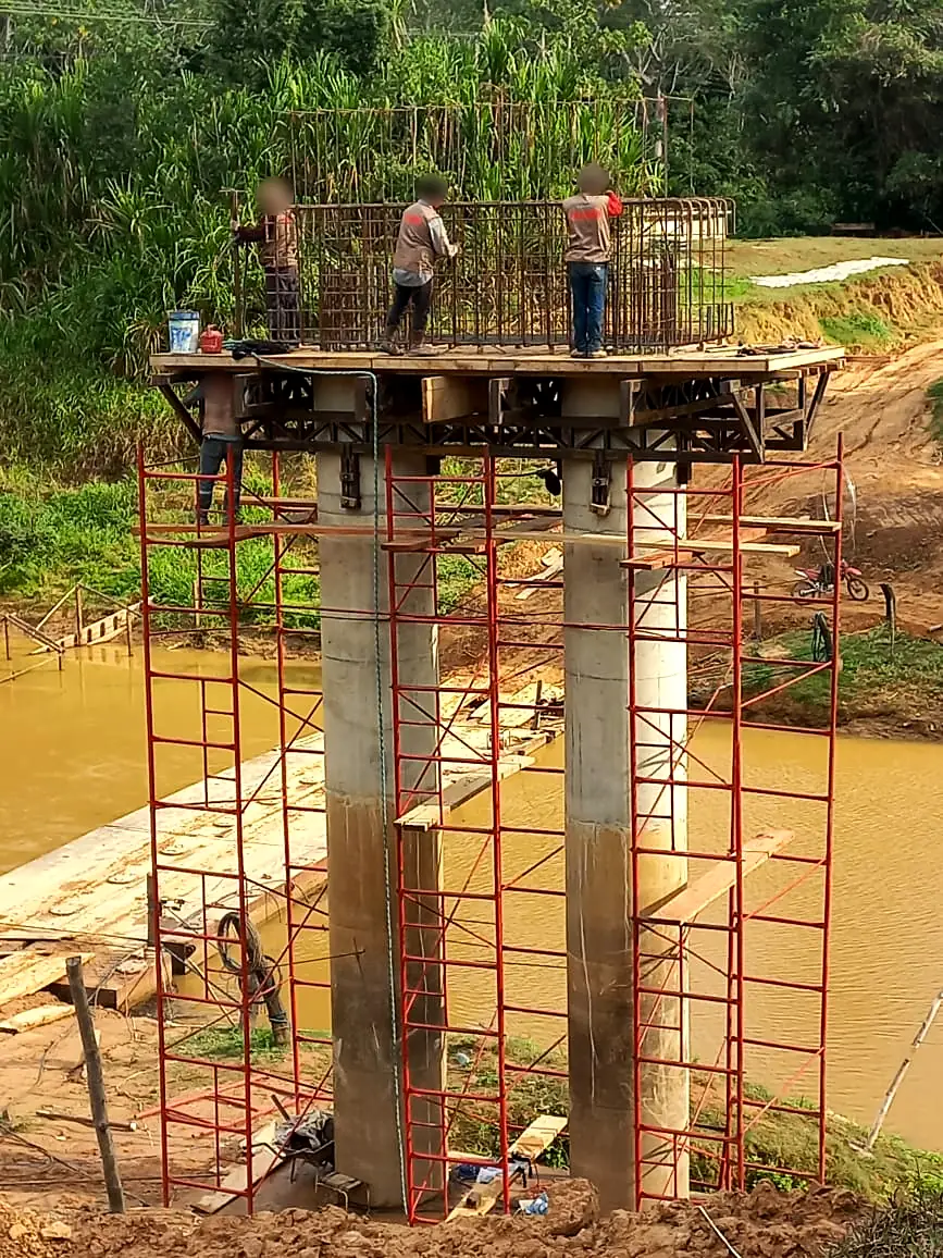 Pila del puente sobre el río Apere con andamios y cuadrilla armando el acero del cabezal (rostros difuminados)